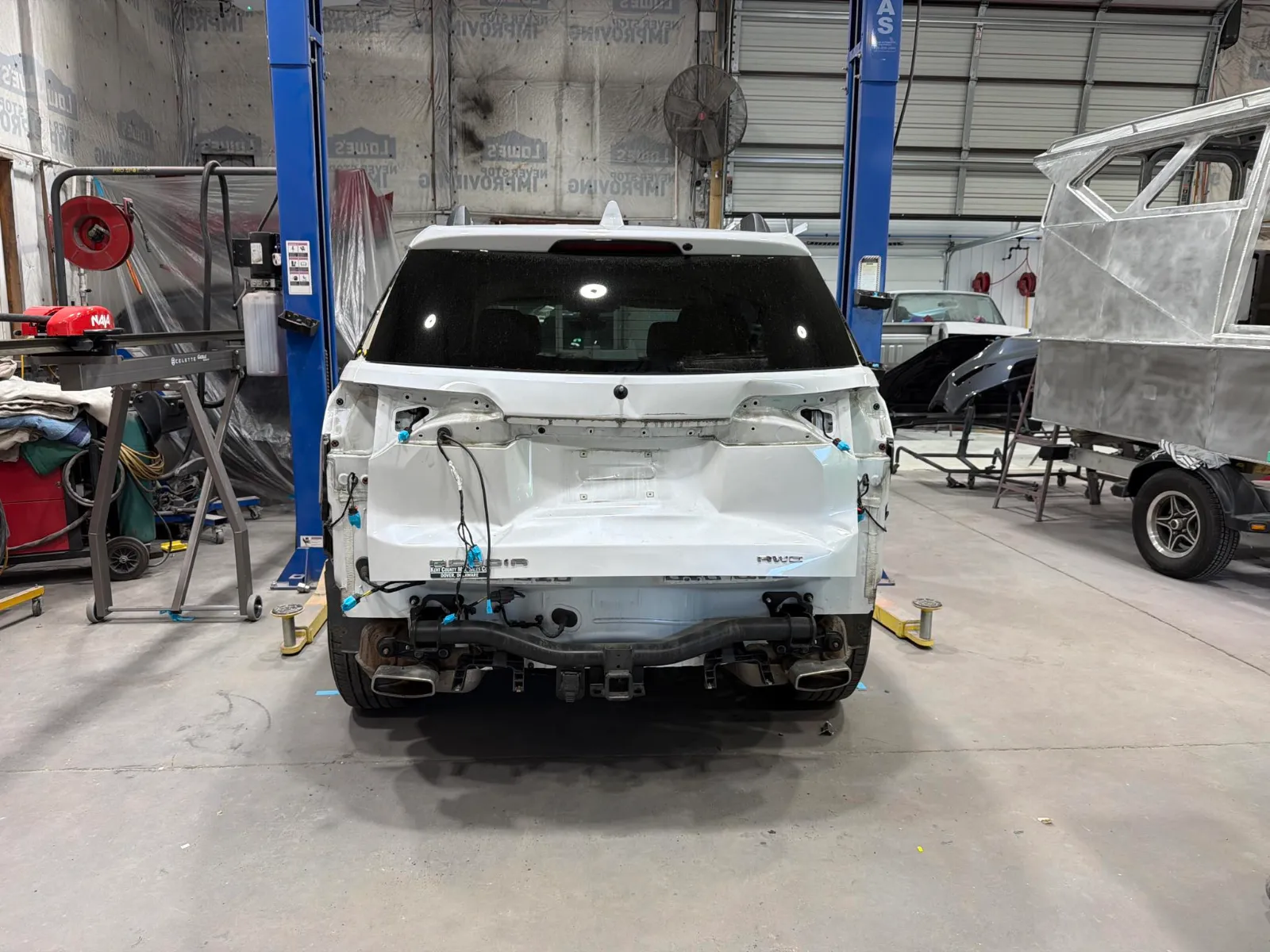 White Ford Bronco on a lift in the Eastern Auto Works shop, rear bumper removed and rear-end damage exposed during repair