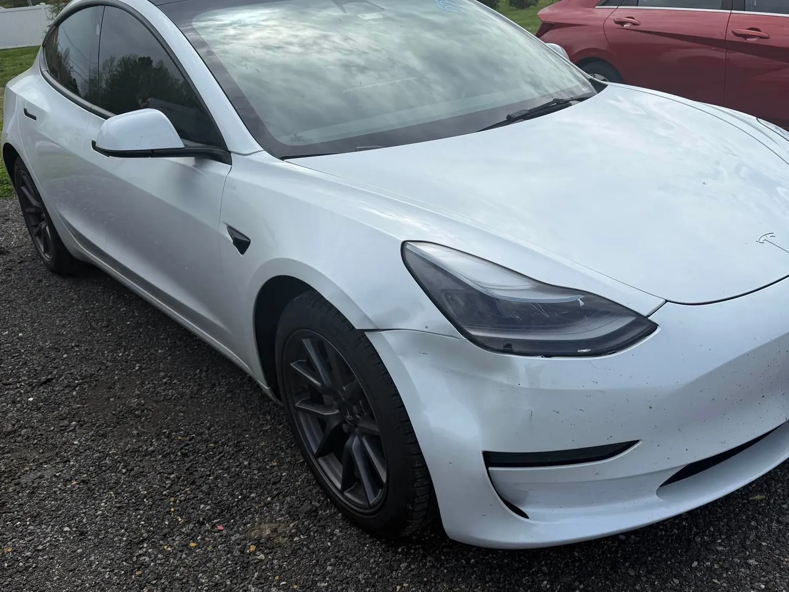 White Tesla sedan before repair, with a damaged front bumper and front fender