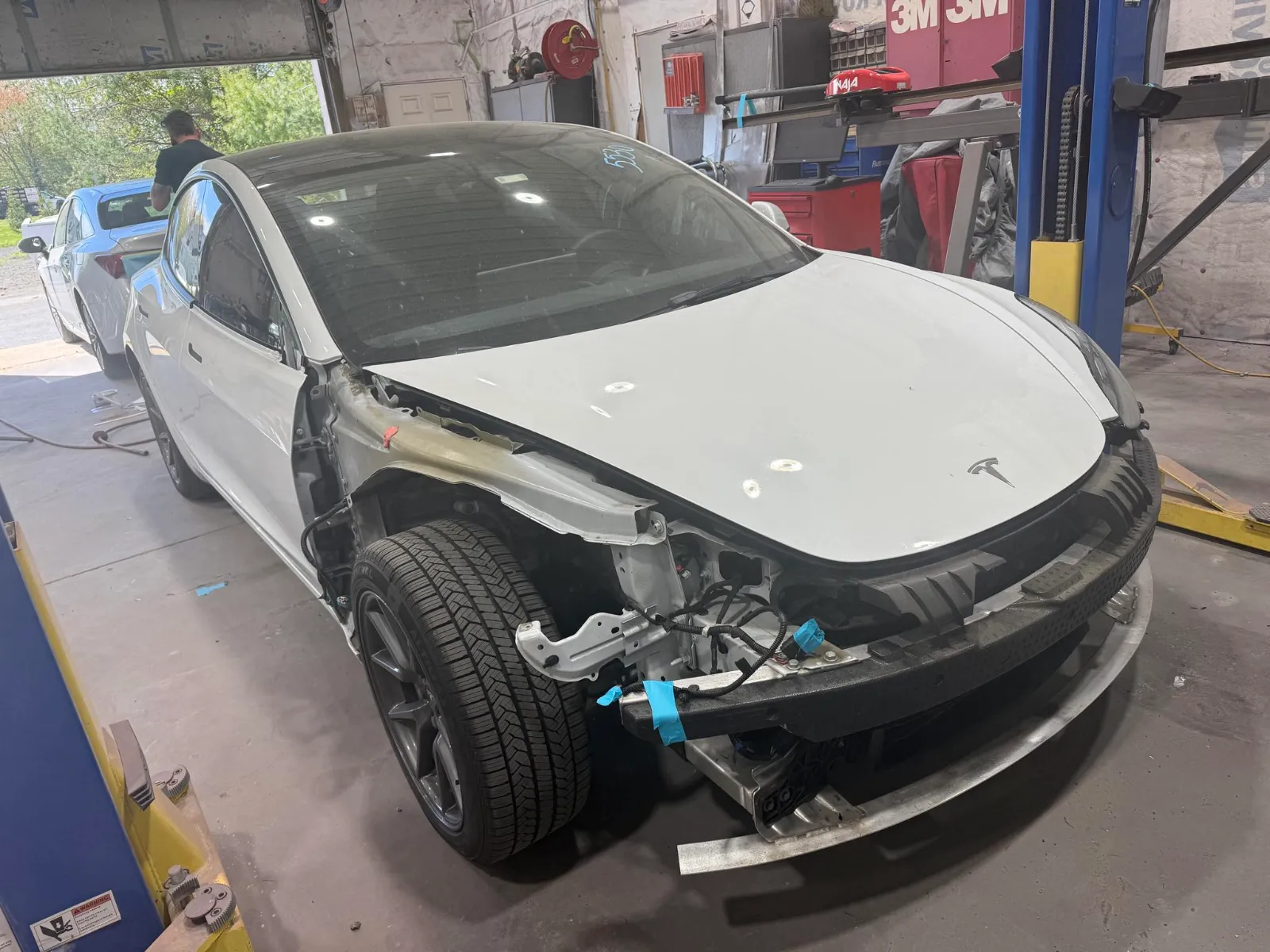 White Tesla sedan in the Eastern Auto Works shop with the front bumper removed during repair