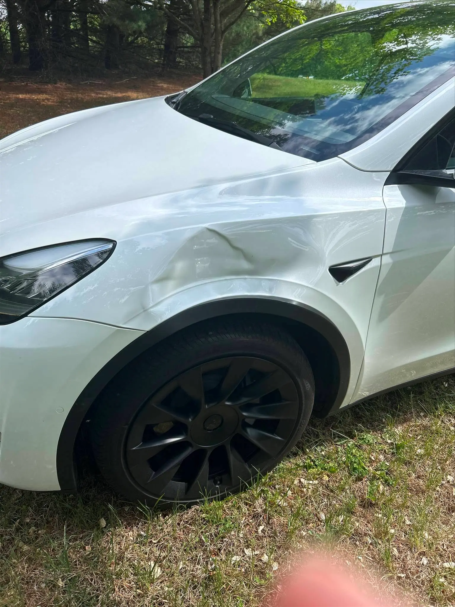 White Tesla before repair, with a dented front fender above the wheel