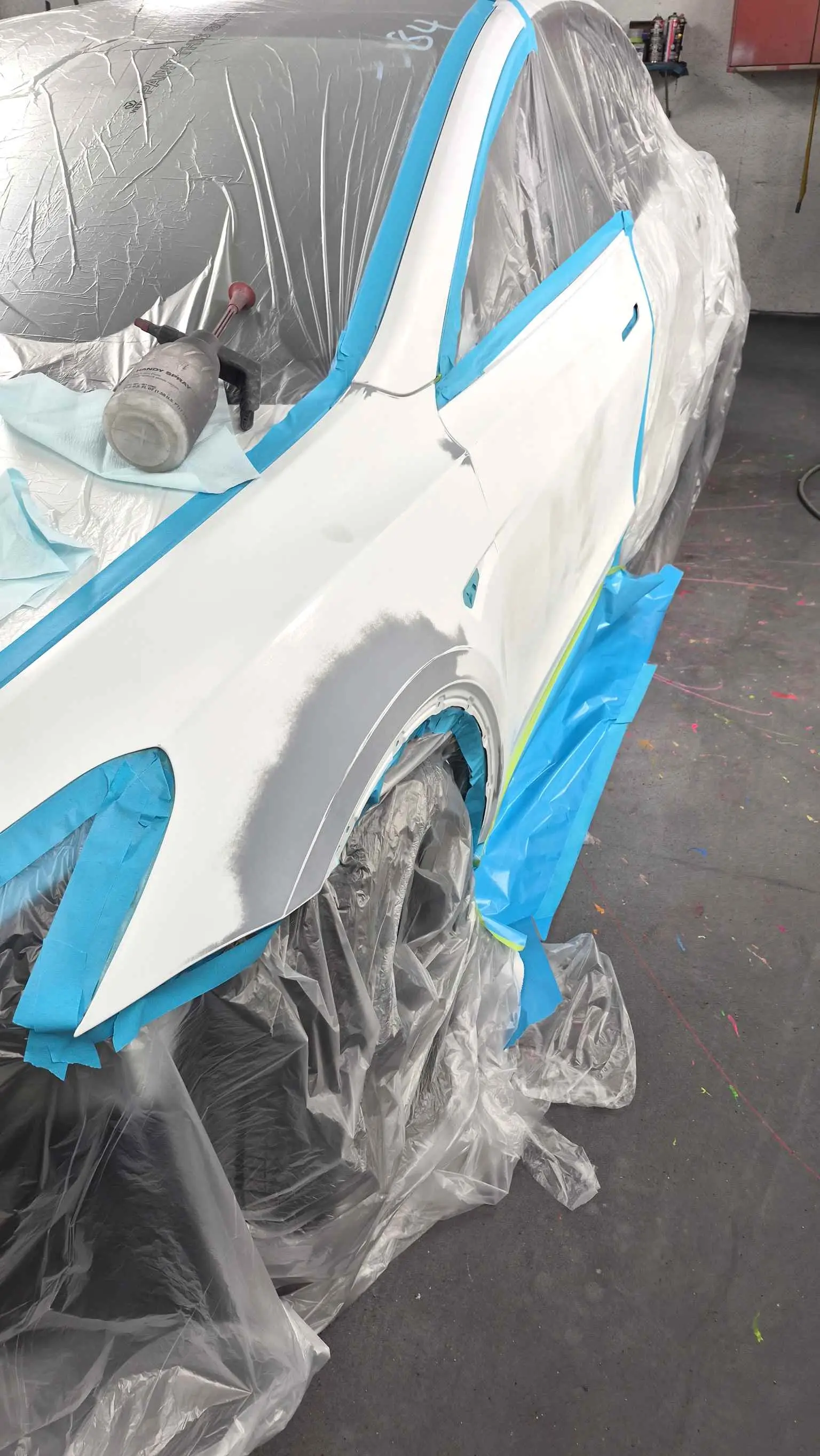 White Tesla fender masked in blue tape and plastic sheeting, prepped for paint